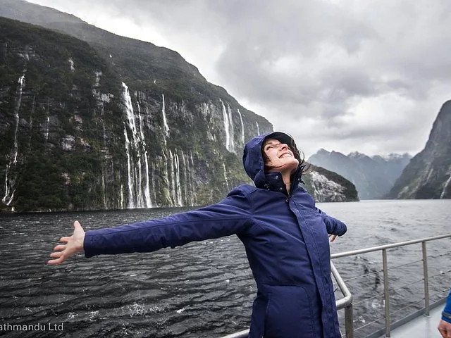 Femme en veste bleue debout sur un bateau, admirant les cascades de Doubtful Sound.