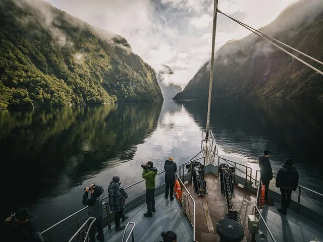 Passagiere blicken von einem Boot auf die Berge und den Nebel im Doubtful Sound.