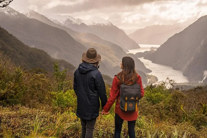 A couple holding hands while viewing Doubtful Sound from a high vantage point.