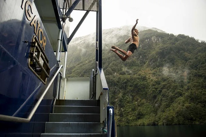 Eine Person springt von der Seite eines Kreuzfahrtschiffs ins Wasser des Doubtful Sound.